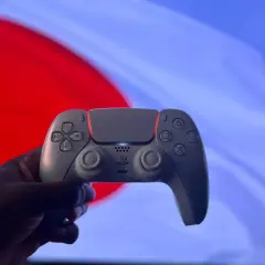 Dłoń trzyma biały kontroler DualSense na tle czerwono-niebieskiego ekranu. Czy gry z PS4 działają na PS5? Tak, większość!