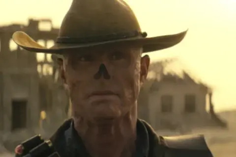 Ghoul z Fallout, w kapeluszu kowbojskim, z bliznami na twarzy, przemierza pustkowia.