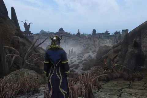 Postać w zbroi i niebieskim płaszczu patrzy na pustynny krajobraz z ruinami w oddali. To Morrowind Remastered.