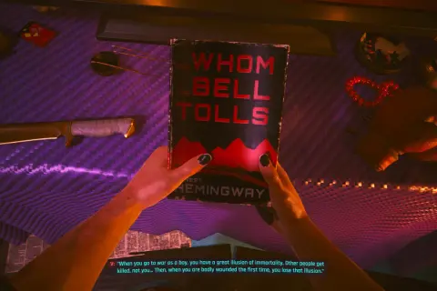 Ręce trzymają książkę "Komu bije dzwon" na tle cyberpunkowego stołu. Jackie z Cyberpunka mógłby czytać tę książkę.
