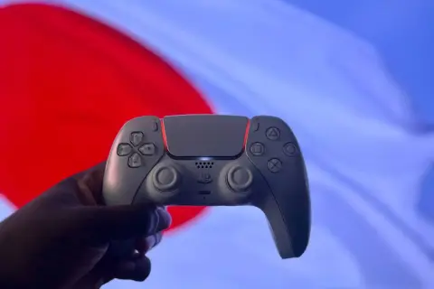 Dłoń trzyma biały kontroler DualSense na tle czerwono-niebieskiego ekranu. Czy gry z PS4 działają na PS5? Tak, większość!