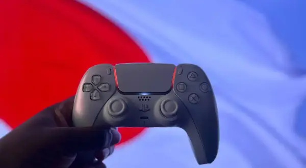 Dłoń trzyma biały kontroler DualSense na tle czerwono-niebieskiego ekranu. Czy gry z PS4 działają na PS5? Tak, większość!