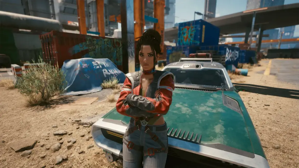 Panam z Cyberpunk 2077 stoi obok swojego zielonego pojazdu, z rękami skrzyżowanymi na piersi, w postapokaliptycznym otoczeniu.