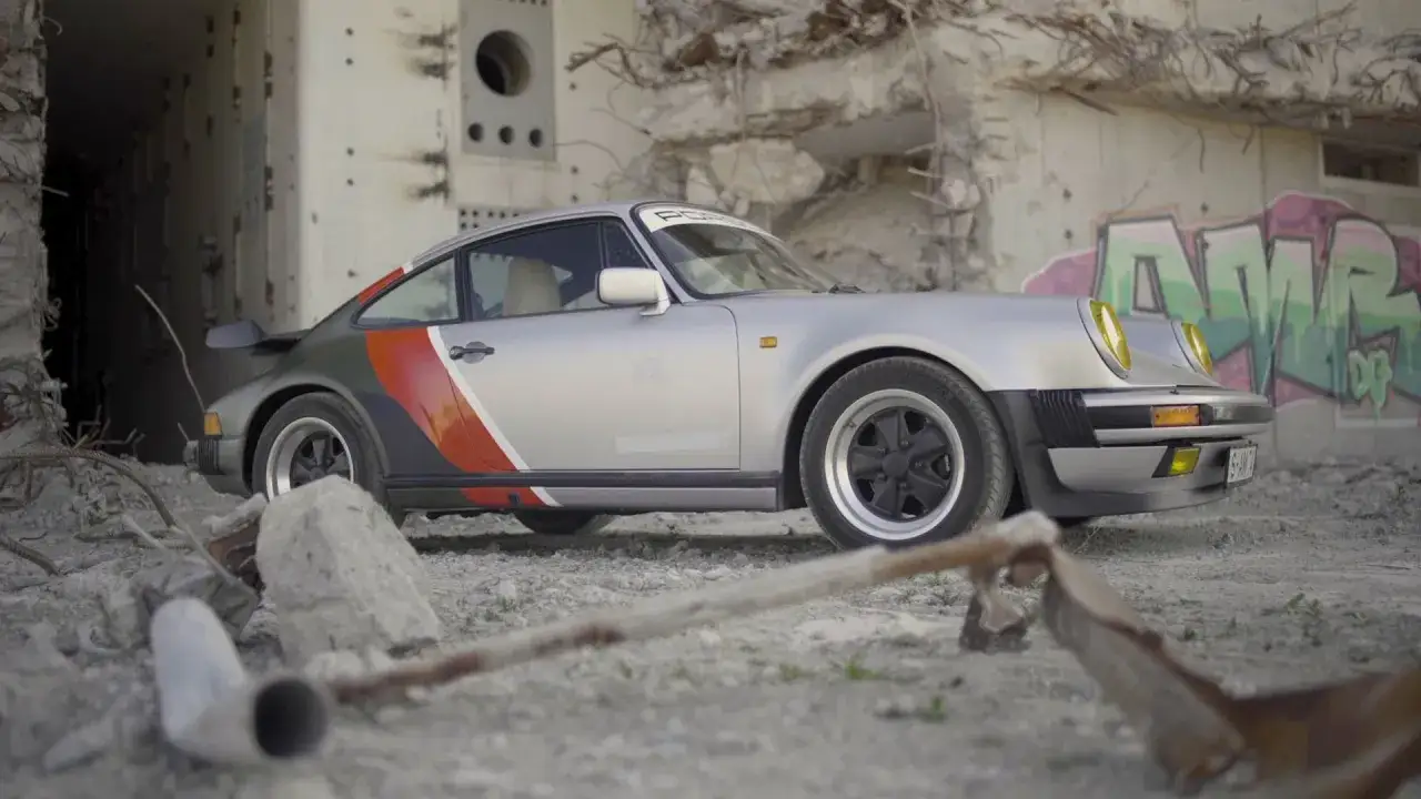 Srebrny cyberpunk Porsche z kolorowymi pasami, stojący wśród ruin i graffiti.