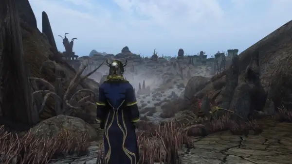 Postać w zbroi i niebieskim płaszczu patrzy na pustynny krajobraz z ruinami w oddali. To Morrowind Remastered.