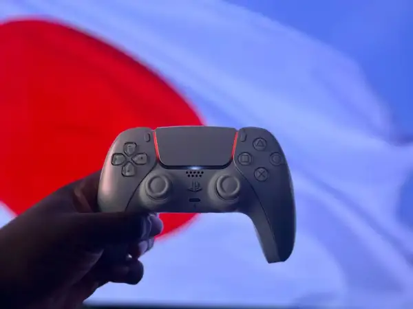 Dłoń trzyma biały kontroler DualSense na tle czerwono-niebieskiego ekranu. Czy gry z PS4 działają na PS5? Tak, większość!